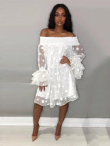 Woman wearing a white off-the-shoulder polka dot dress with ruffled bell sleeves and nude heels