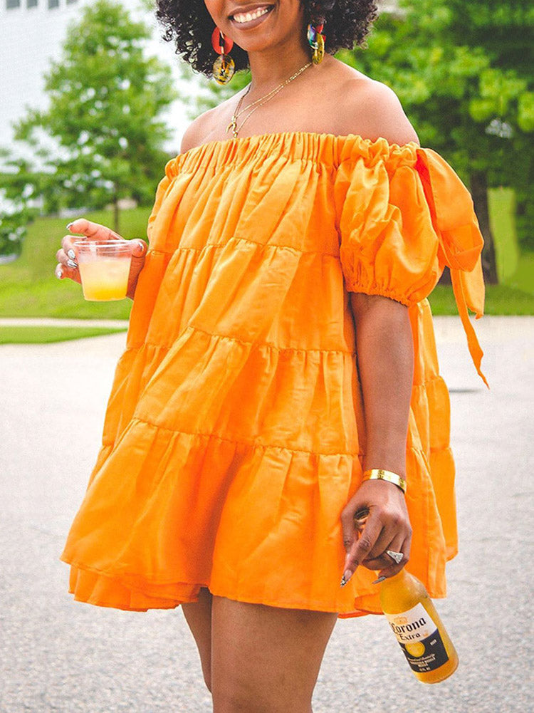 Woman wearing an orange off-the-shoulder tiered mini dress with puff sleeves and holding a drink.