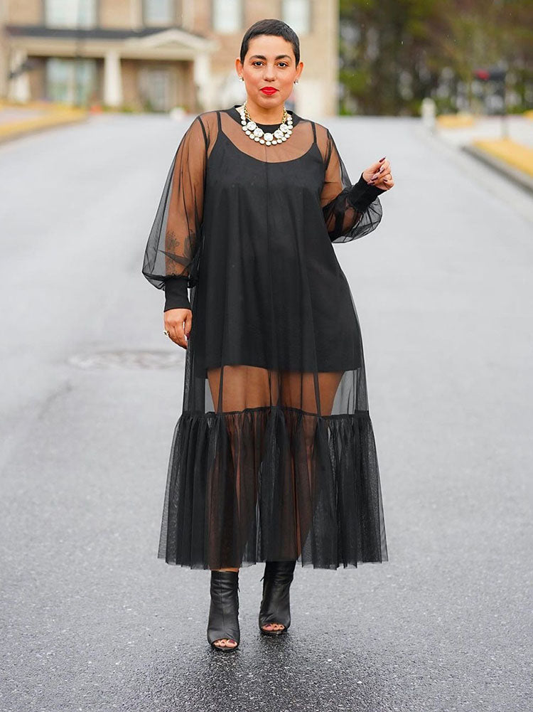 Woman wearing a black sheer midi dress with balloon sleeves and a tiered hem.
