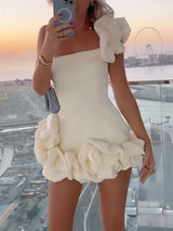 Woman holding a phone, taking a selfie in a white one-shoulder mini dress with ruffled embellishments.