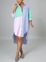 Woman wearing a colorblock striped button-down shirt dress with a high-low hem and blue heels, posing against a grey background.