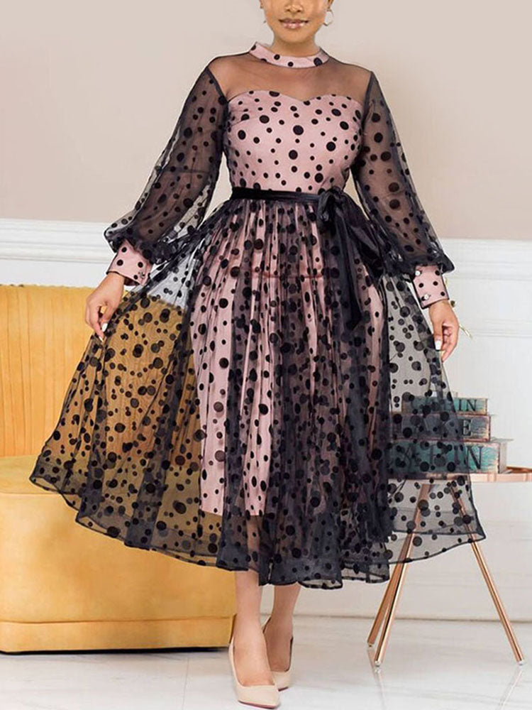 Woman wearing a pink and black polka dot midi dress with sheer sleeves and a belted waist.