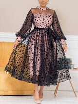 Woman wearing a pink and black polka dot midi dress with sheer sleeves and a belted waist.
