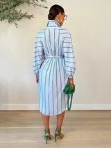 Back view of a woman wearing a light blue and green striped shirt dress with a belted waist and balloon sleeves.