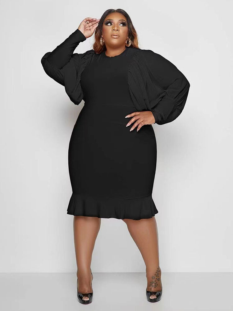 Woman in a black dress with puff sleeves and a ruffle hem, posing with hand on hip.