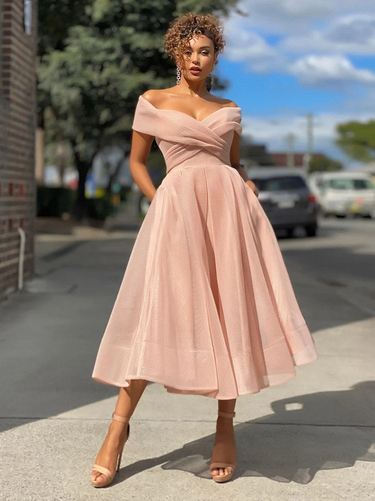Woman wearing a blush pink off-the-shoulder A-line dress with a cinched waist and flared skirt, standing outdoors.