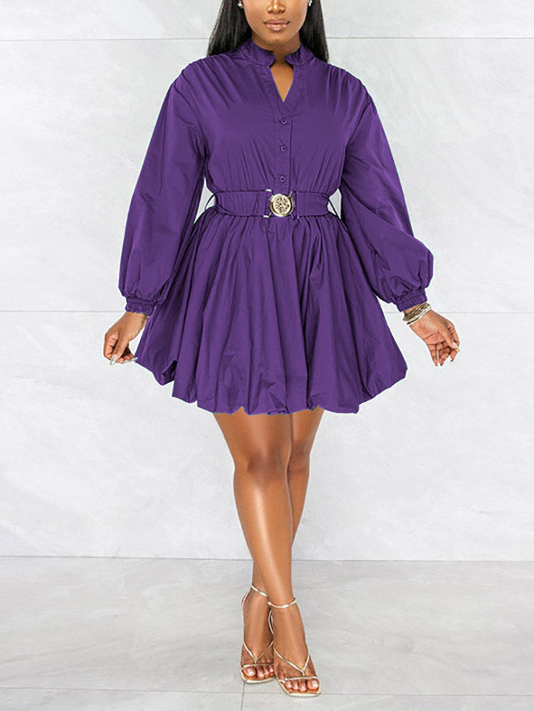 Front view of a woman wearing a purple fit and flare dress with balloon sleeves and a decorative belt, standing against a marble background.