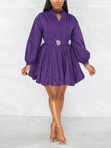 Front view of a woman wearing a purple fit and flare dress with balloon sleeves and a decorative belt, standing against a marble background.