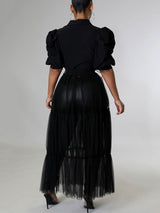 Back view of a woman wearing a black maxi dress with puffed sleeves and a tiered tulle skirt over black pants