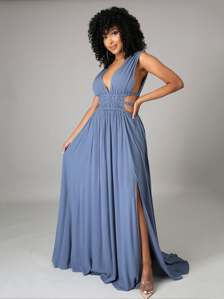 Woman in a blue sleeveless maxi dress with a plunging V-neck, cut-out waist details, and a high slit, standing with one hand on her hip.