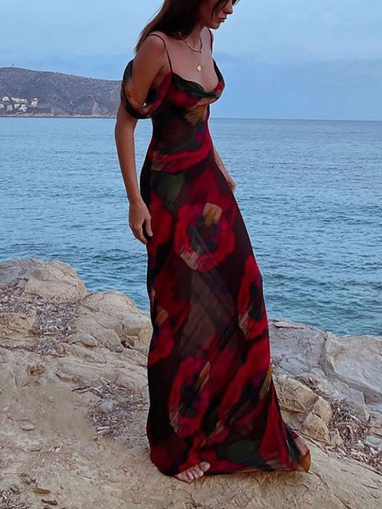 Woman wearing a long abstract floral print dress with cold shoulder sleeves standing on rocks by the sea.