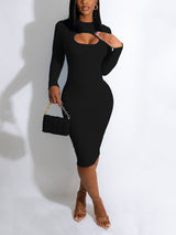 Woman wearing a black long-sleeved ribbed midi dress with a cut-out detail at the chest, holding a small black quilted handbag and wearing nude strappy heels.