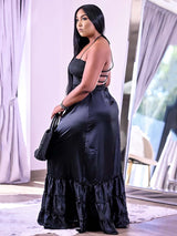 Side view of a woman in a black satin maxi dress with a halter neckline and ruffled hem.