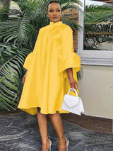 Woman wearing a yellow A-line dress with bell sleeves and a high neckline, holding a white handbag.