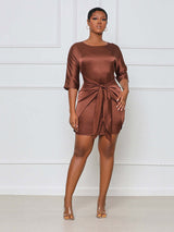 Woman wearing a brown satin mini dress with a tie waist and round neckline from the front.