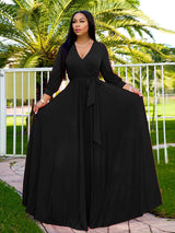 Woman wearing a long black wrap dress with a V-neck and long sleeves, standing outdoors with palm trees in the background.