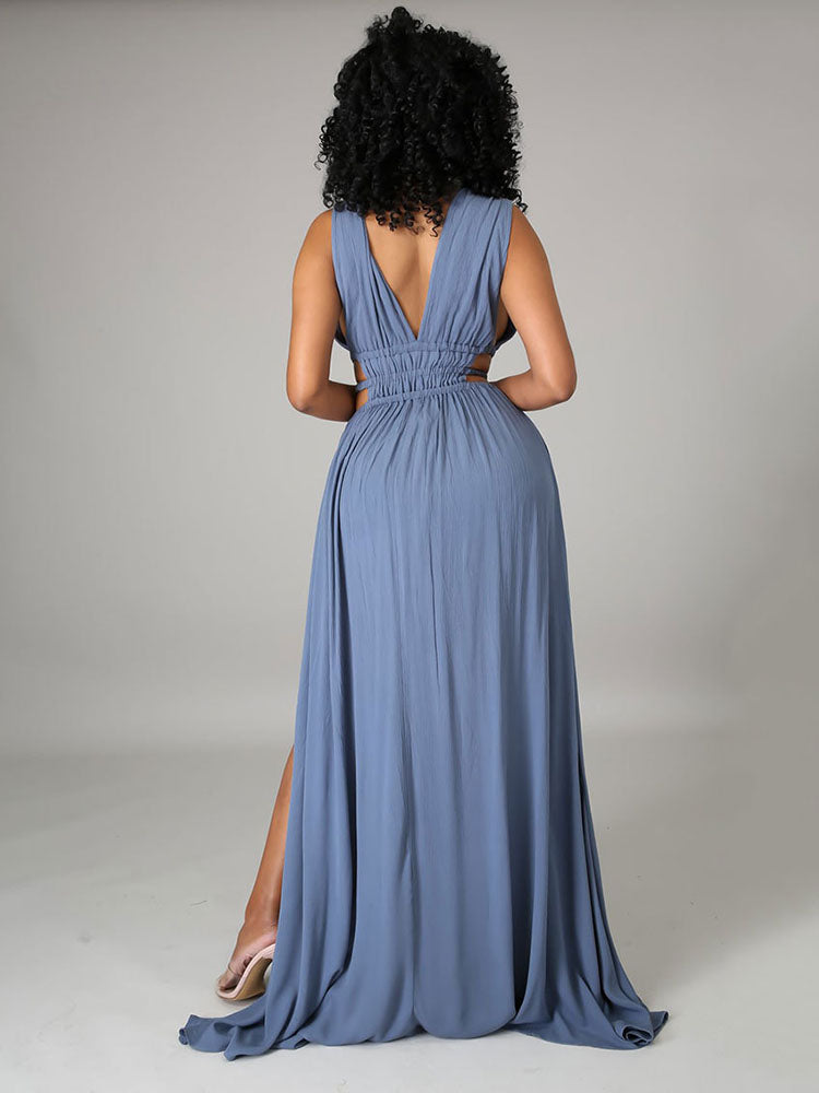 Back view of a woman in a blue sleeveless maxi dress with a deep V-back, cut-out waist details, and a high slit.