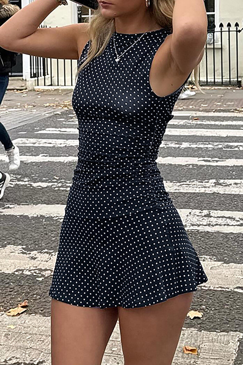 Woman posing in a navy polka dot mini dress on a street.
