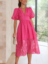 Front view of a woman wearing a vibrant pink midi dress with a V-neck and puff sleeves, showcasing the button-down detail and sheer grid overlay.