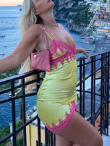 Woman posing on a balcony in a yellow slip dress with pink lace trim, with a coastal town and ocean in the background.