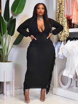 Woman wearing a black maxi dress with fringe detailing and a deep V-neck.