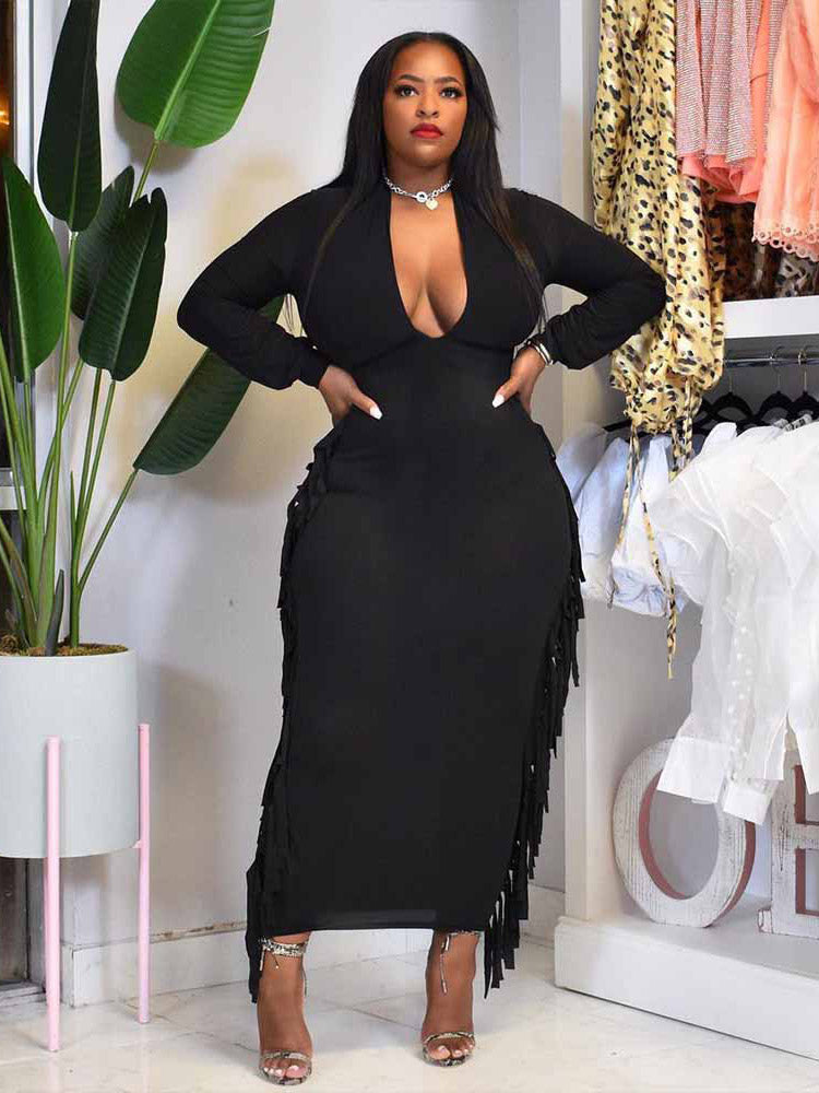 Woman wearing a black maxi dress with fringe detailing and a deep V-neck.