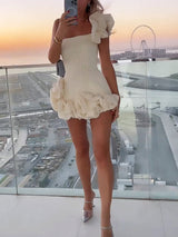 Full body shot of a woman in a white one-shoulder ruffled mini dress and sparkling heels.