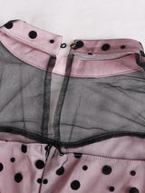 Close-up of the neckline and sheer mesh detail on a pink and black polka dot dress.