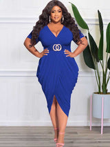 Plus-size model in a royal blue ruched V-neck short-sleeve dress with a tulip hem and side slit, accessorized with a gold double-ring belt and hoop earrings.