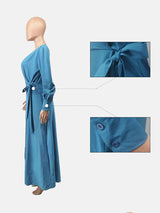 Side view of a woman wearing a teal long-sleeve maxi dress with a belted waist and high slit