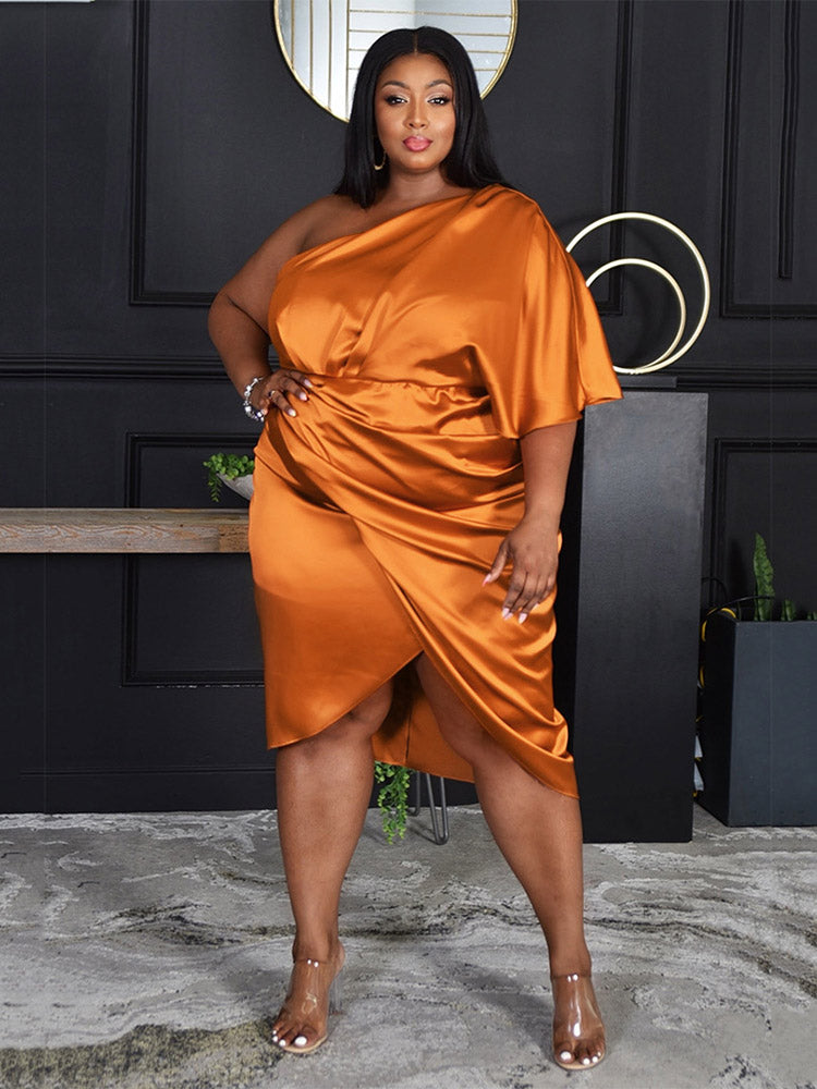 Woman wearing an orange satin one-shoulder dress with a draped bodice and tulip hem skirt, posing with her hand on her hip.
