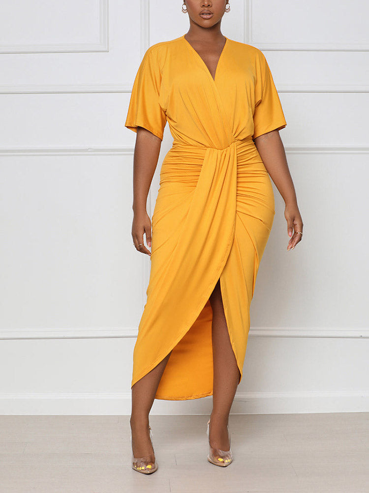 Woman wearing a yellow V-neck wrap dress with short sleeves, ruched waist, and asymmetrical hem with a slit.