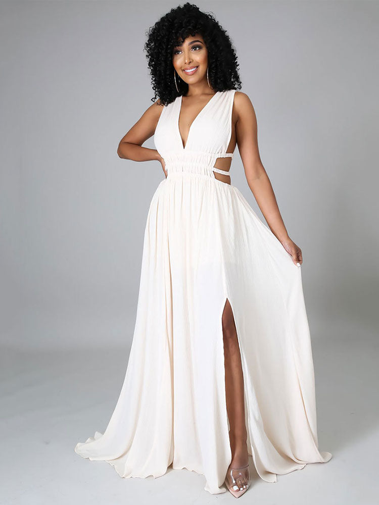 Woman in an off-white sleeveless maxi dress with a plunging V-neck, cut-out waist details, and a high slit, posing with a hand on her skirt.