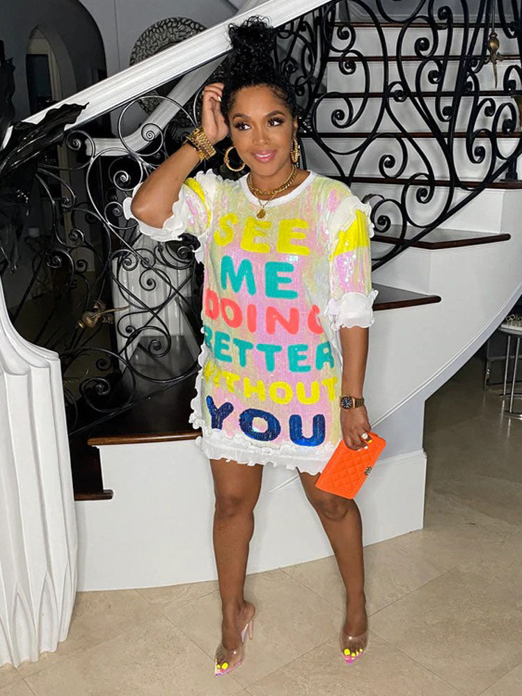 Woman wearing a white sequined t-shirt dress with colorful text that reads 'SEE ME DOING BETTER WITHOUT YOU'.
