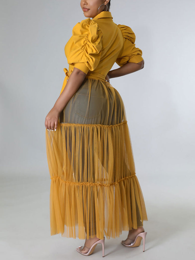 Back view of a woman wearing a mustard yellow maxi dress with puffed sleeves and a tiered tulle skirt