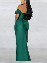 Back view of a woman in a floor-length emerald green off-the-shoulder dress with draped detailing