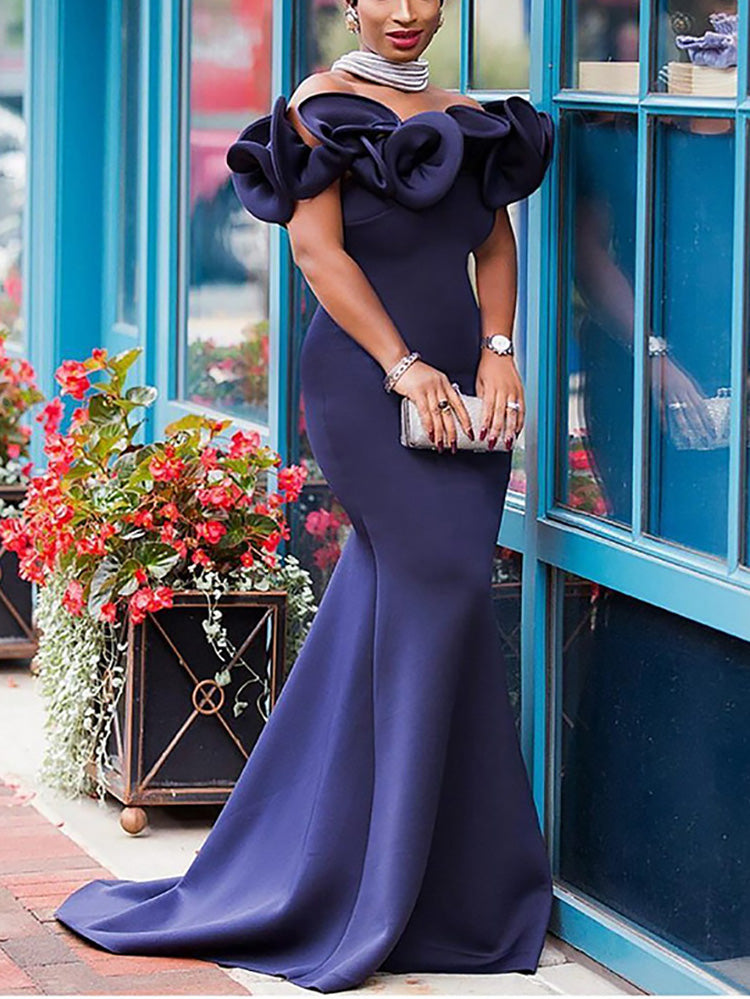 Woman wearing a navy blue off-the-shoulder formal gown with ruffle shoulder details and a mermaid train.