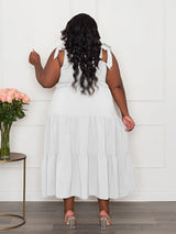 Back view of a plus-size woman wearing a white tiered maxi dress with tie shoulder straps and a smocked bodice.