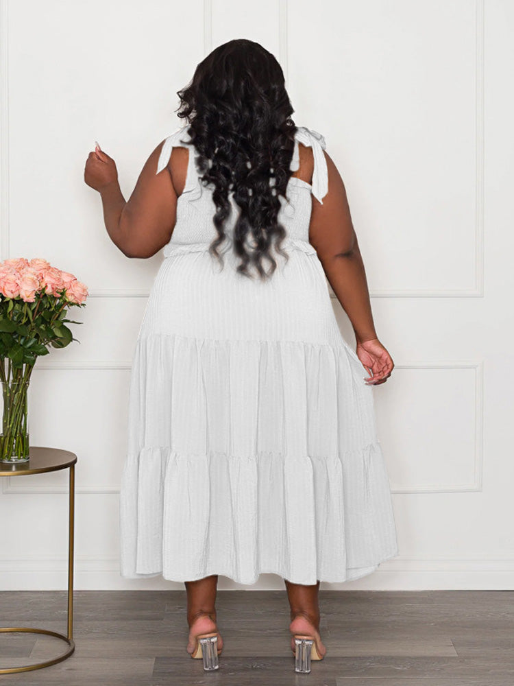 Back view of a plus-size woman wearing a white tiered maxi dress with tie shoulder straps and a smocked bodice.