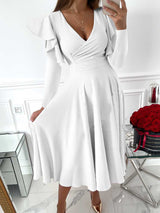 woman wearing a white V-neck dress with ruffled long sleeves and a flared skirt