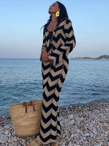Full body shot of a woman in a black and beige chevron knit maxi dress by the ocean