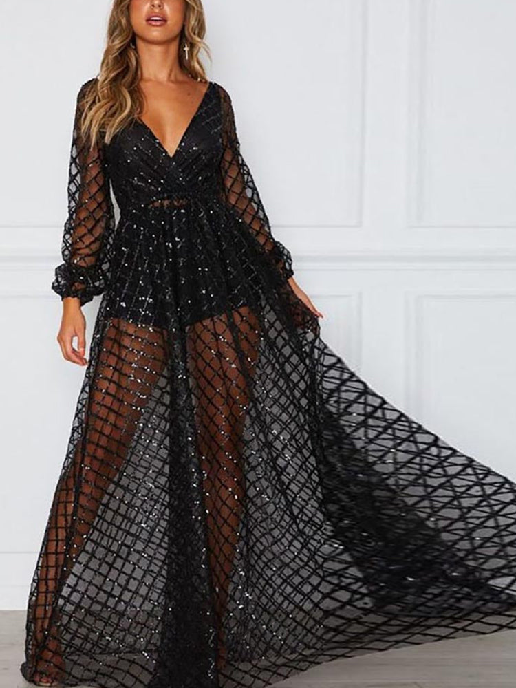 Woman in a long, sheer, sparkling black dress with long sleeves and a V-neck, posing indoors.