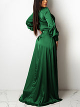Rear view of a woman in a forest green satin wrap maxi dress with a high slit and long puff sleeves.