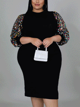 A woman models a black sheath dress with sequin embellished bishop sleeves and a mock neckline.