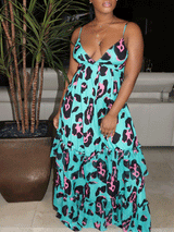 Woman standing next to a potted plant, wearing a turquoise maxi dress with a black and pink leopard print, featuring spaghetti straps, a plunging v-neck, and a tiered, ruffled skirt.