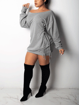 Woman wearing a light grey off-the-shoulder mini dress with drawstring details and long sleeves, paired with black knee-high boots.