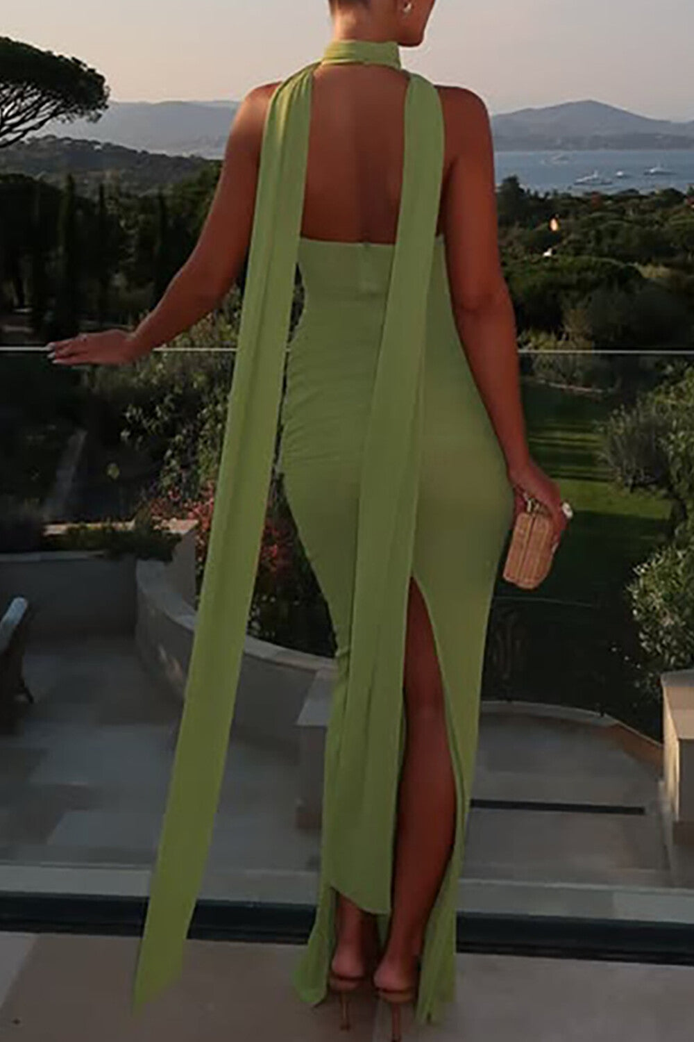 Rear view of a woman in a lime green halter maxi dress with a tie-front detail and high slit, showing the open back.