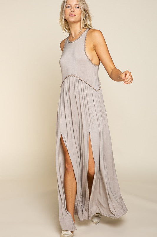 woman wearing a grey sleeveless maxi dress with high side slits and a decorative neckline trim