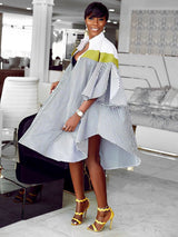Full-body shot of a woman in a voluminous, striped shirt dress with a green accent, showcasing the asymmetrical hemline.