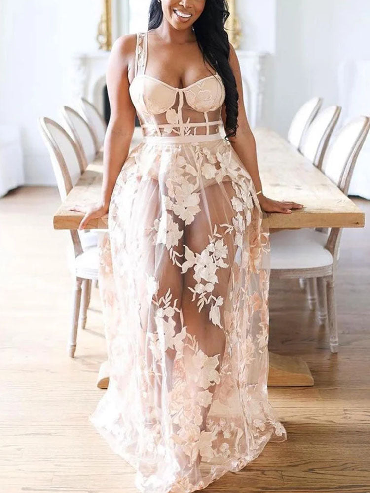 Woman in a sheer floral embroidered maxi dress with a corset-style bodice, sitting at a dining table.